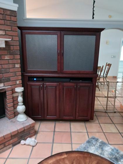 Cherry media armoire with textured glass doors beside a brick fireplace