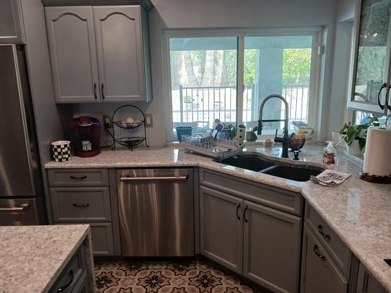 Painted gray kitchen cabinets around a corner sink and dishwasher
